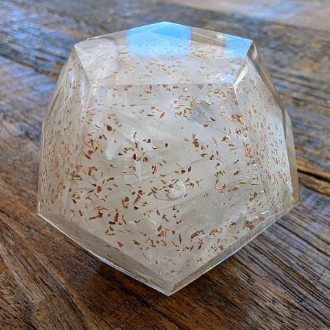 A clear twelve-sided crystal with copper flecks inside, held in a hand