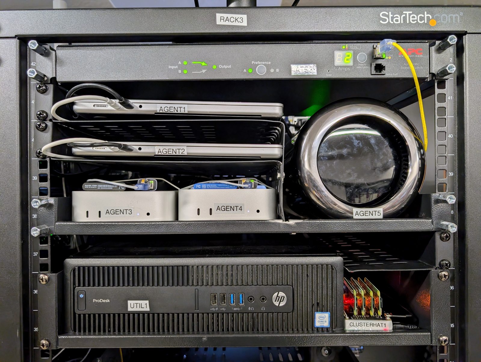 Laptops and small-form computers on a rack shelf, lids open, cables gathered to one side