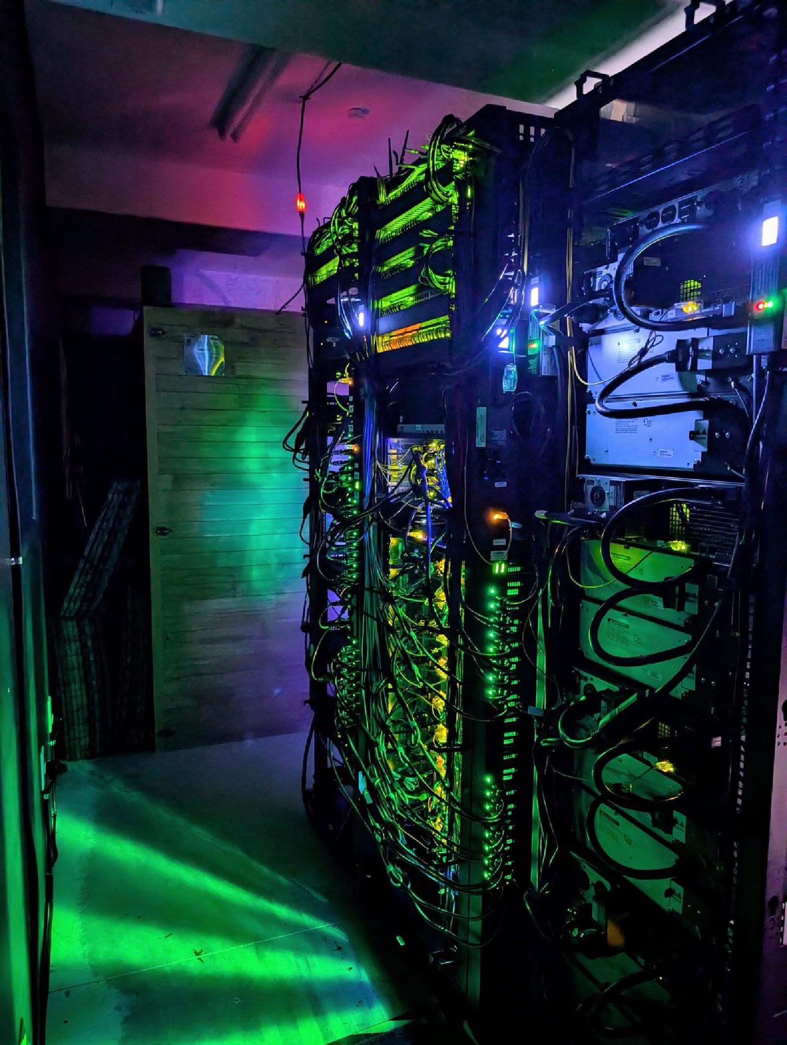The rear of two racks in the dark, cable bundles lit green from the switch ports