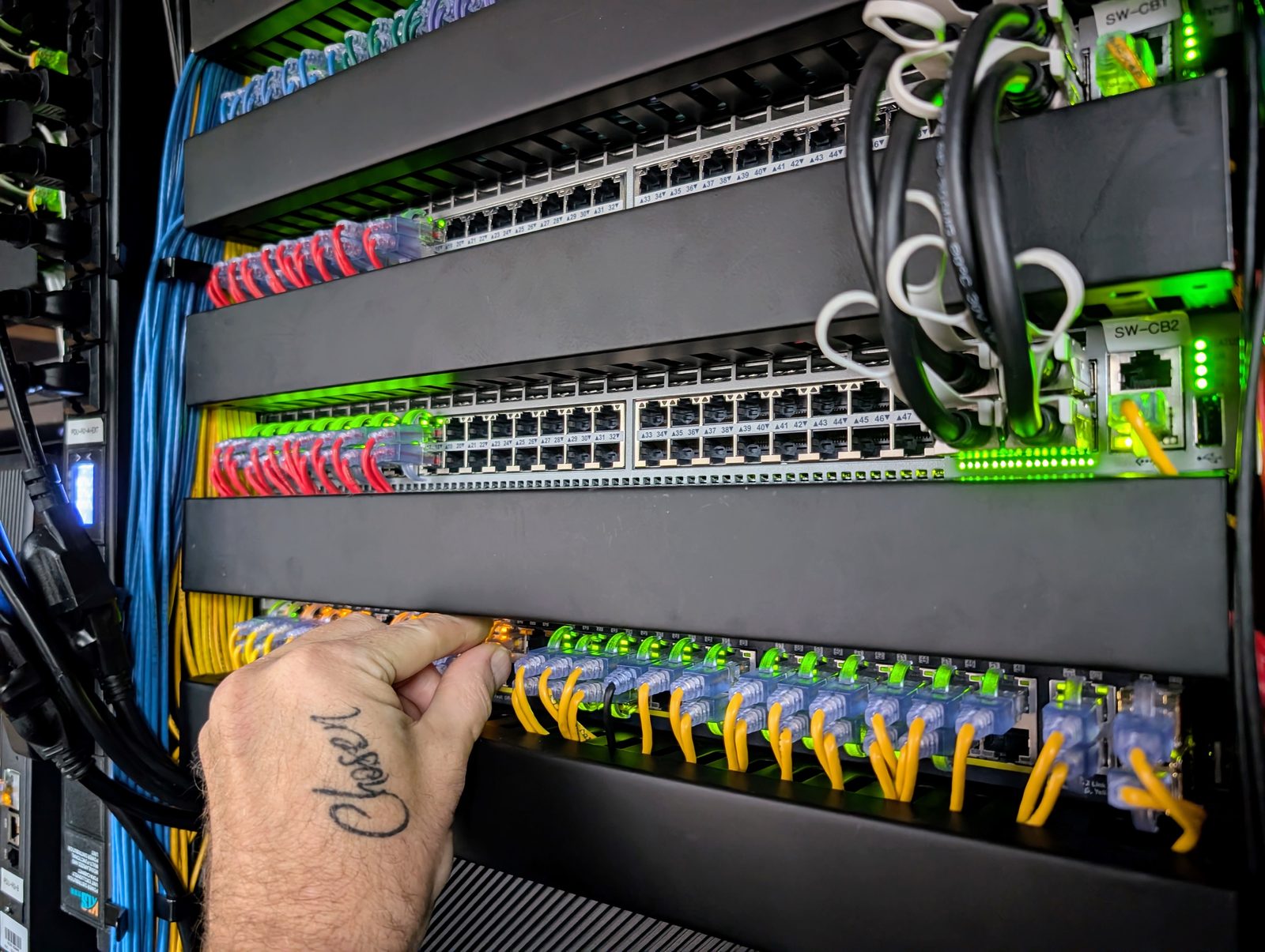 A hand seating a cable in a patch panel, the switch ports lit green behind it