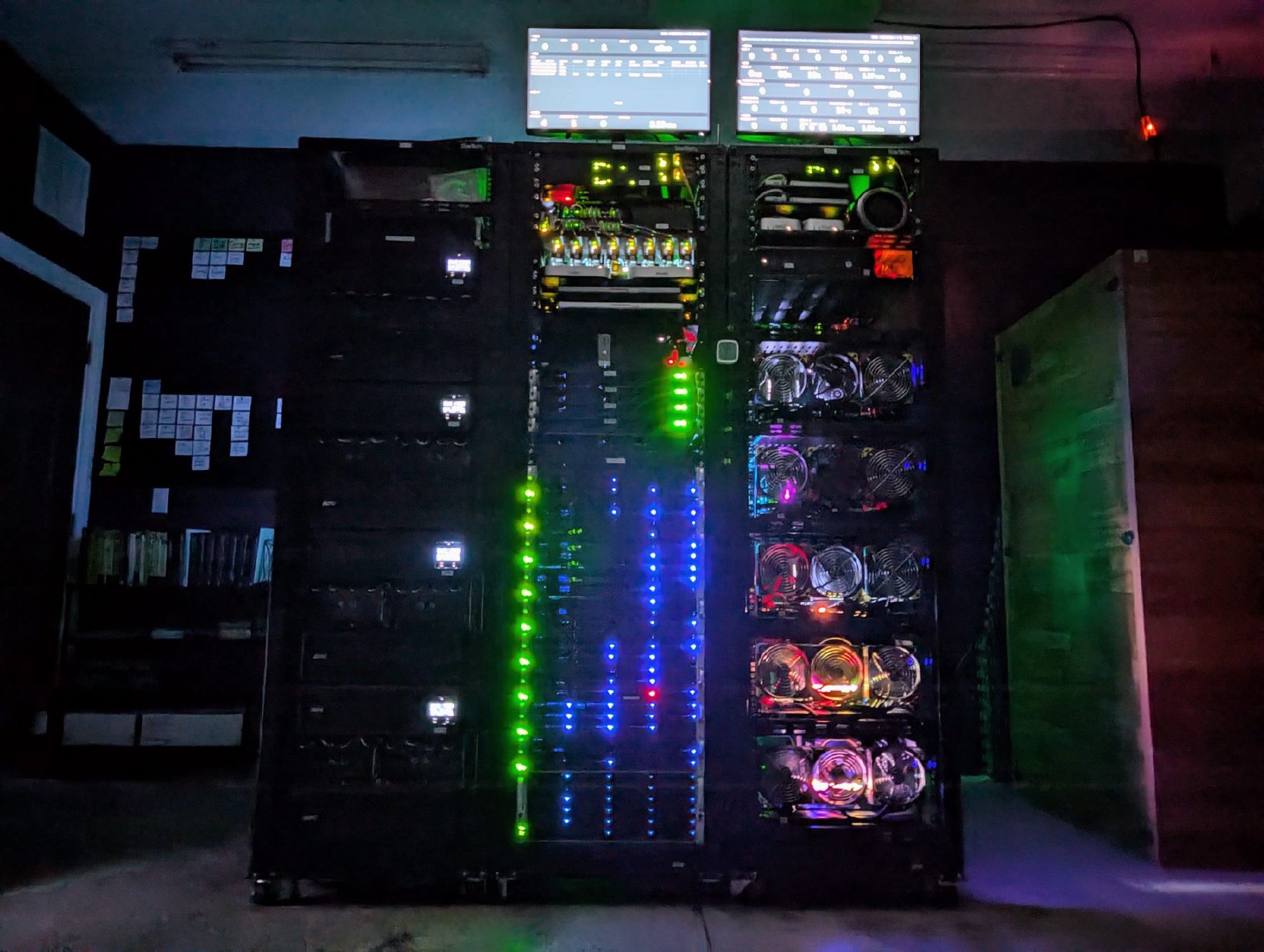 Three server racks in a dark room, lit by their own LEDs and the two dashboards mounted above them