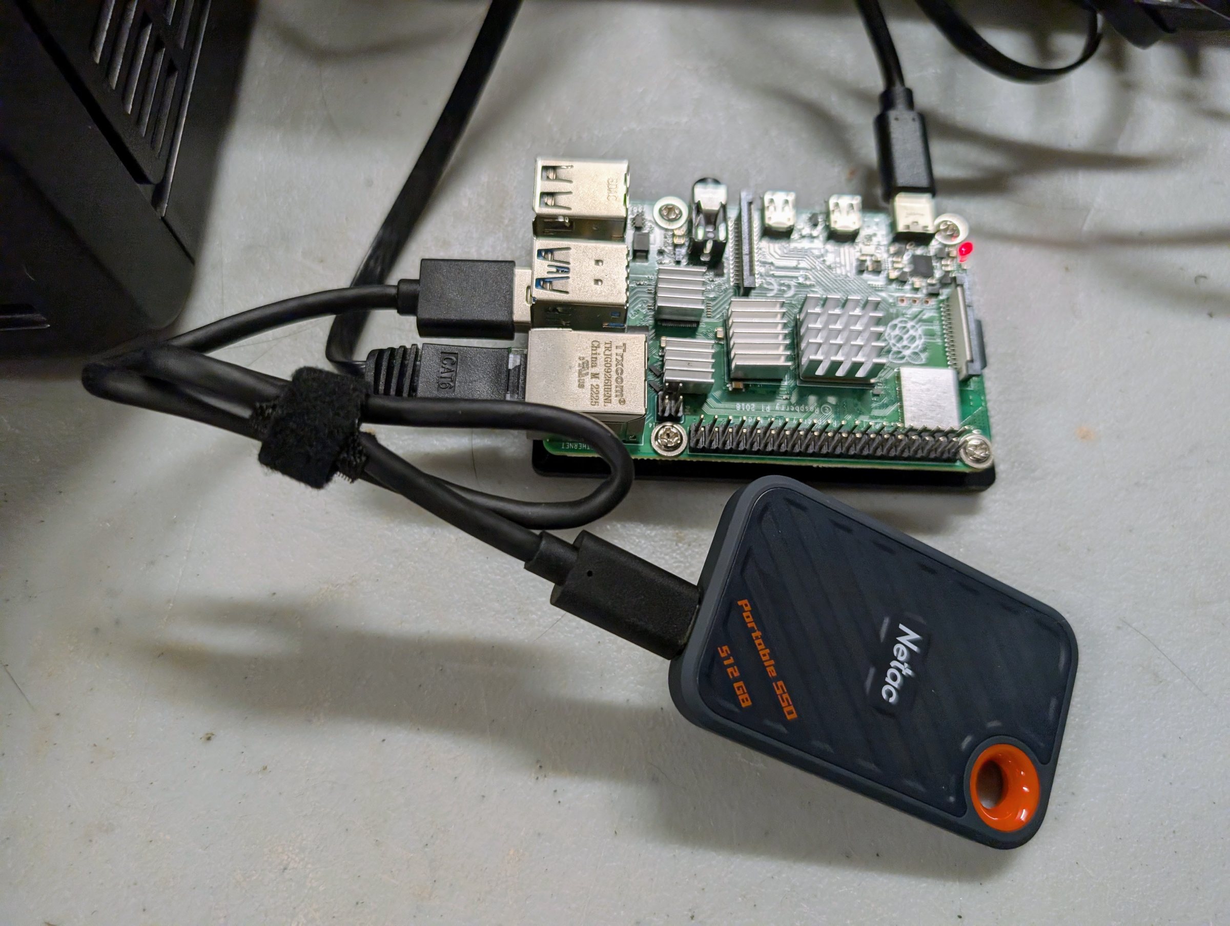 A bare Raspberry Pi 4 board with heatsinks, a network cable and a short USB cable to a small portable SSD lying beside it.