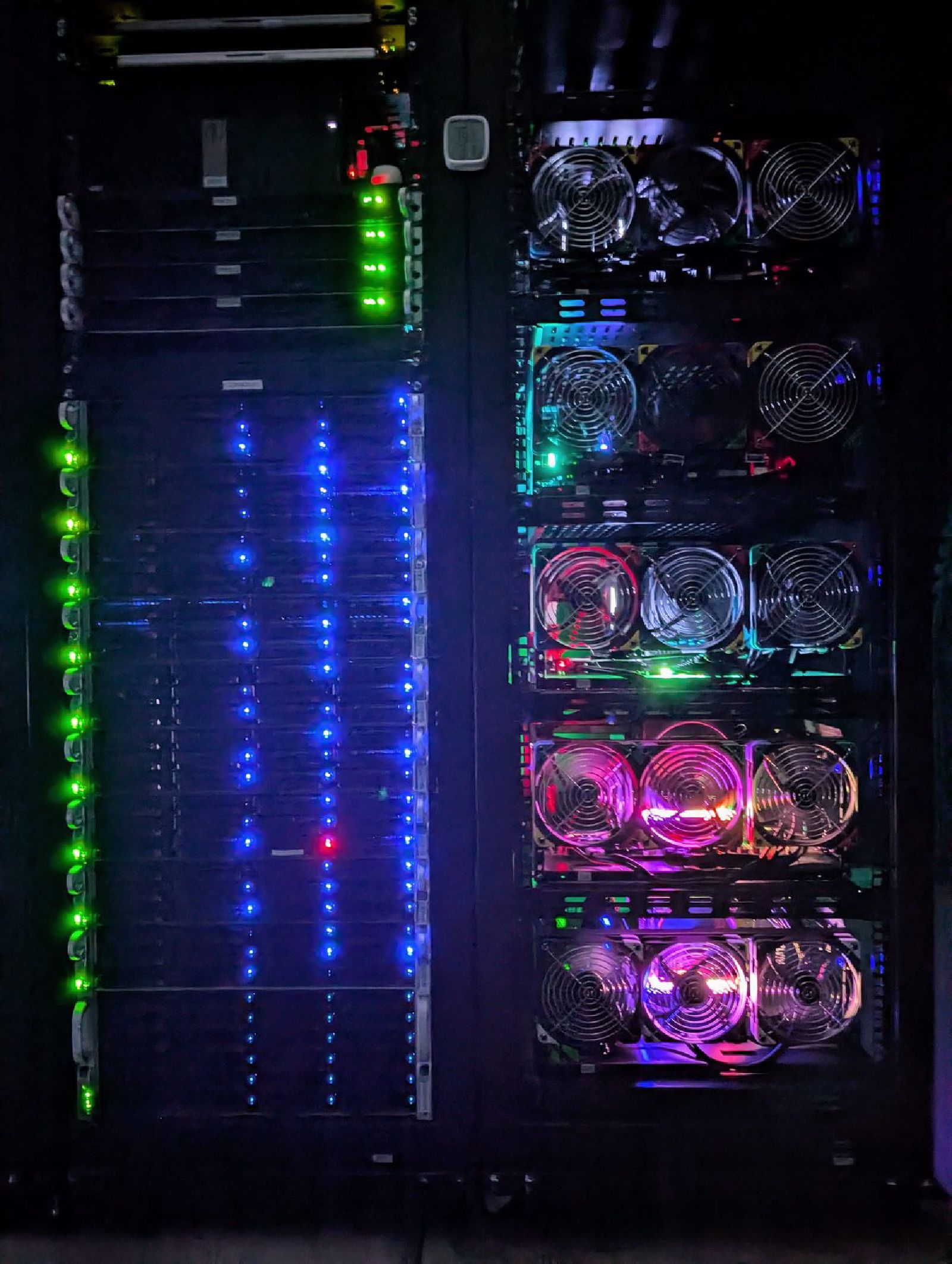 Racks 2 and 3 in the dark: drive lights in blue down the storage wall, the fan rings of the DI servers glowing beside them