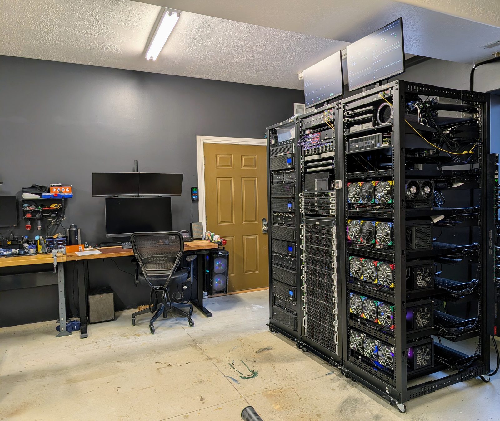 A desk and chair in the foreground, server racks standing along the wall behind them